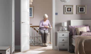 Mujer en un salvaescaleras Stannah en lo alto de las escaleras del primer piso de la casa